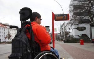 Junger Mann im Rollstuhl und Smartphone in der Hand