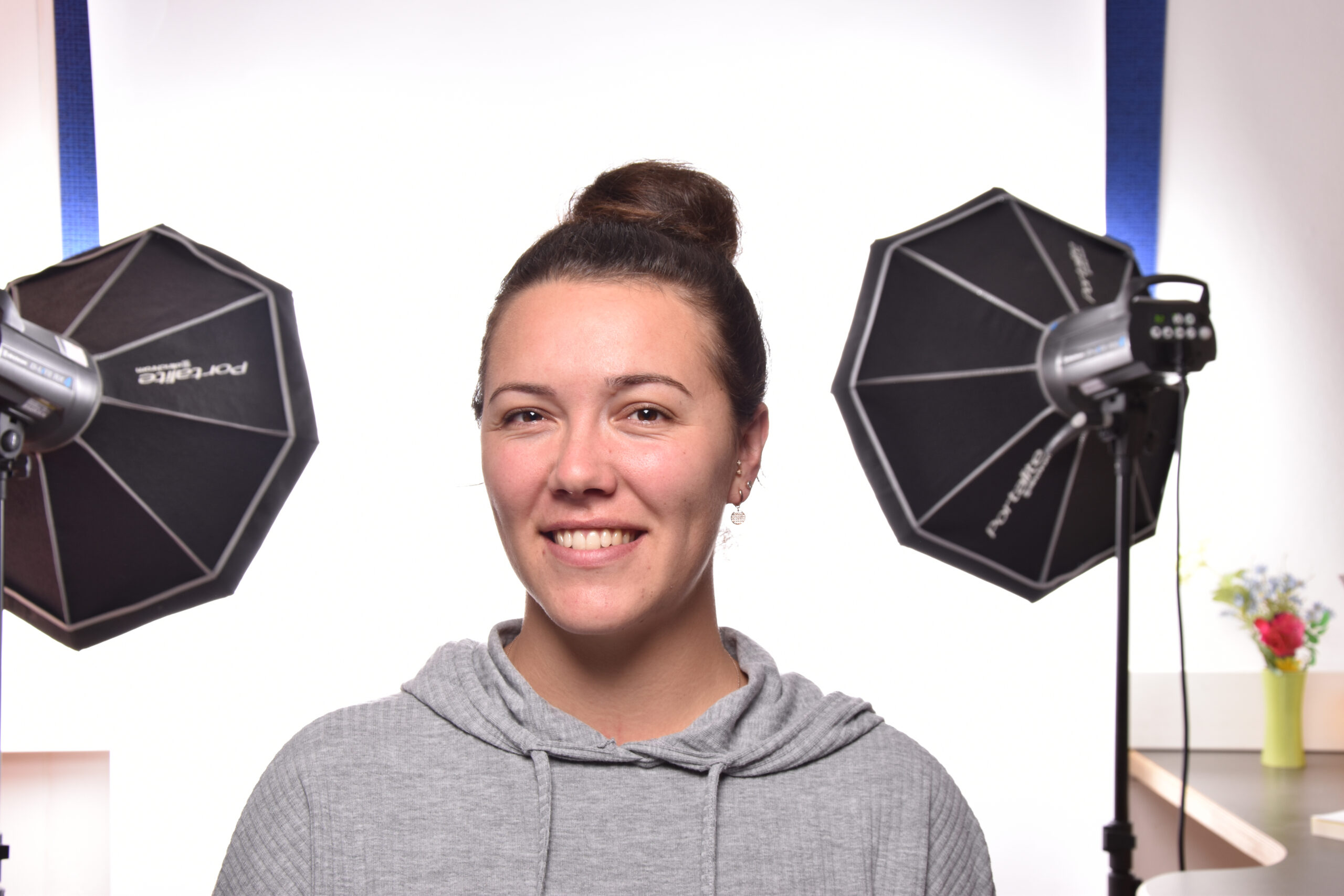 Portrait Veronika Girtner lächelnd, mit Graue Hoodie und Studio Beleuchtung hinter sich